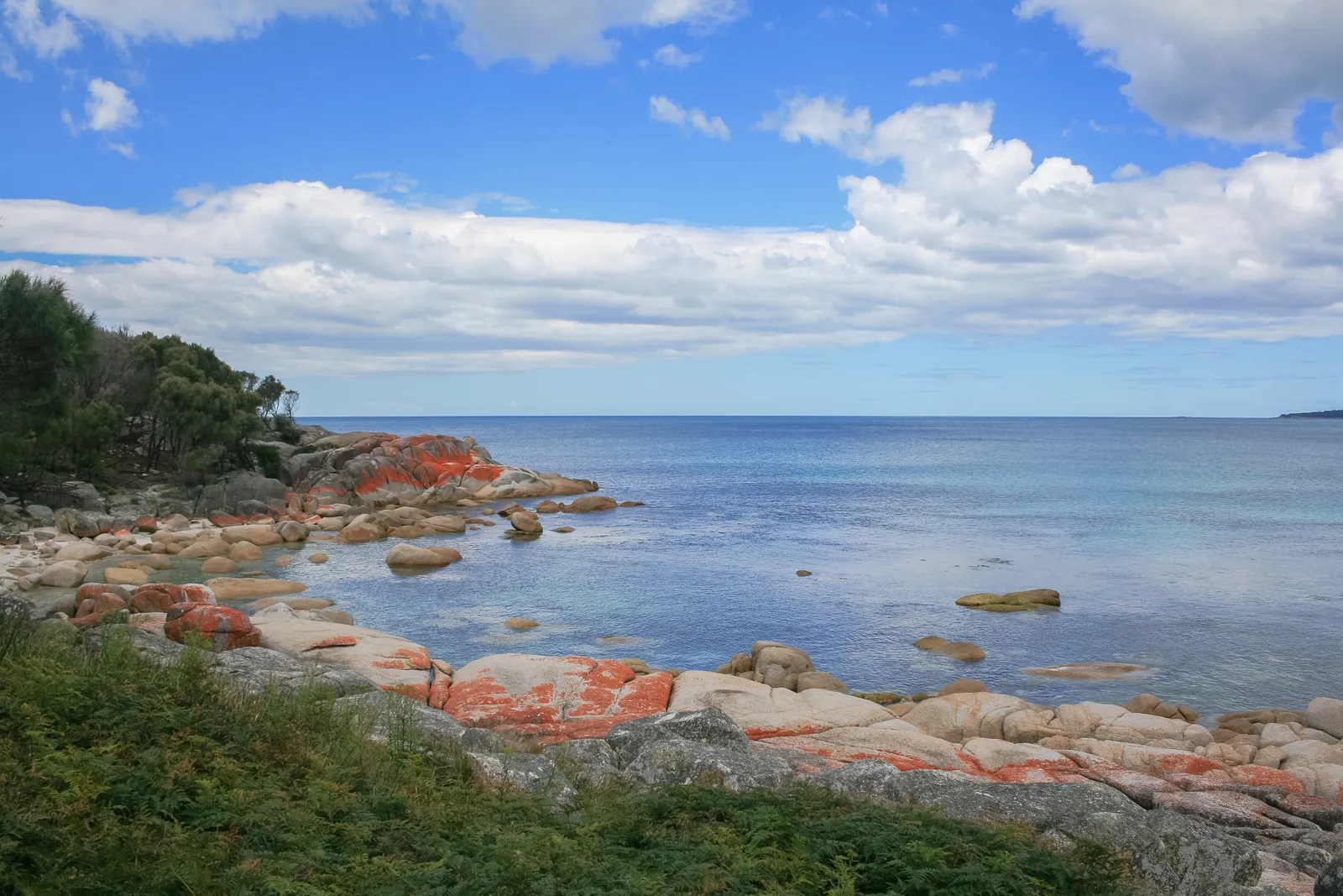 Orange lichen-covered granite rocks beside clear water in the Bay of Fires, Tasmania