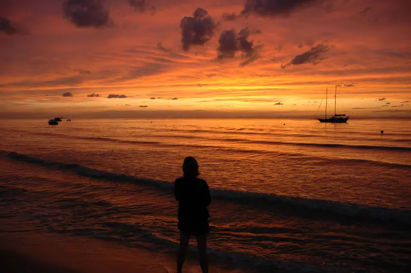 A person standing on the seashore at sunset on Moreton Island, with boats in view