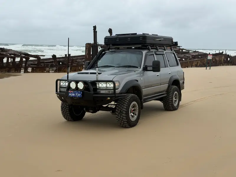 An off-road SUV parked on the beach at K'gari beside a shipwreck