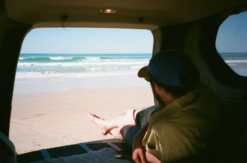 A man relaxing in the open boot of a car on Rainbow Beach