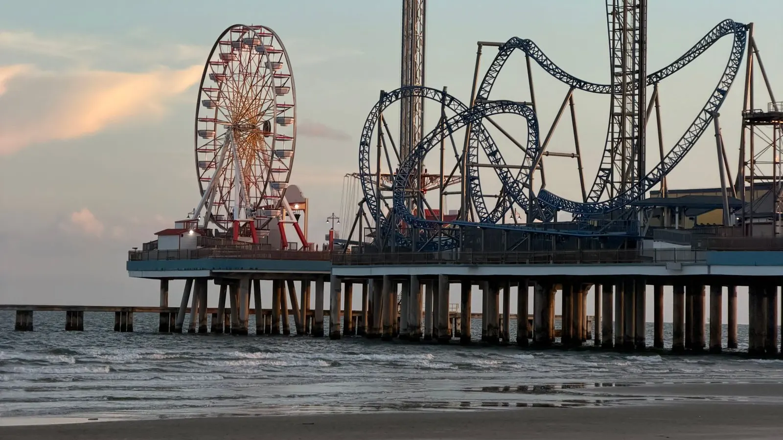 Galveston's Pleasure Pier at dusk, with the Ferris wheel, drop tower and roller coaster above the surf
